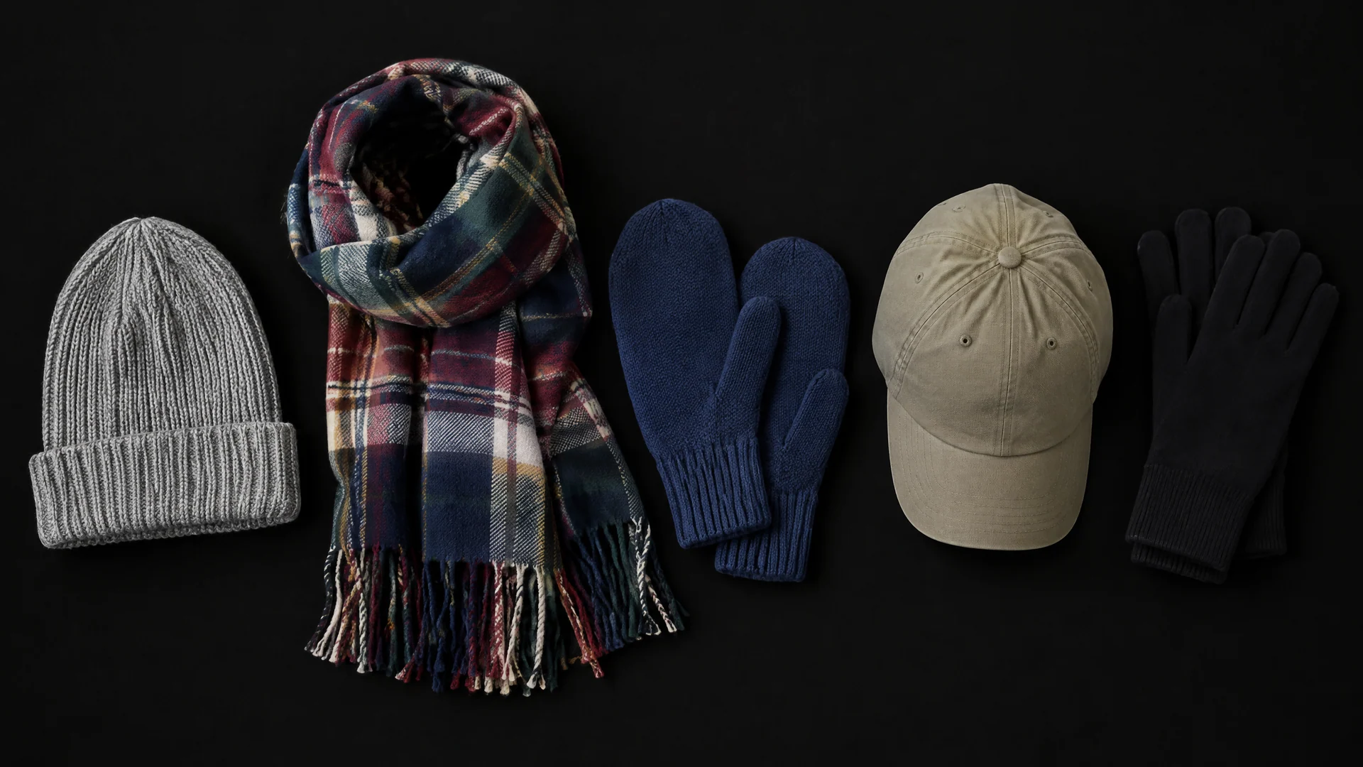 Ribbed beanie, plaid scarf, navy mittens, khaki cap and black gloves in a row on a black background